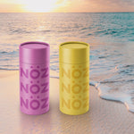 Load image into Gallery viewer, Nöz reef-safe sunscreen sticks in yellow and purple on a beach.
